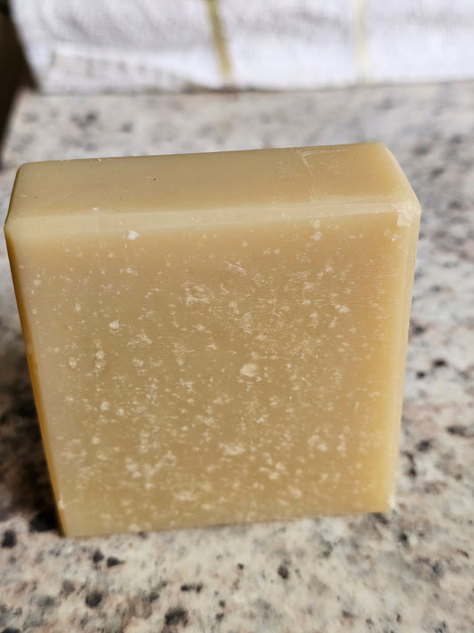 Pale golden Bare Veil Goat Milk Soap bar, Jenny’s Favorite, standing on a stone countertop.